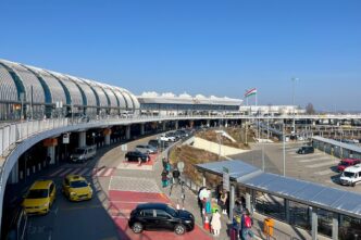 Під’їзна дорога до терміналу аеропорту Будапешт Ференц Ліст: автомобілі біля входу, пасажири з валізами та угорський прапор над будівлею