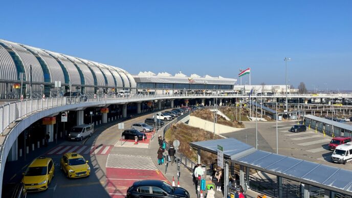 Під’їзна дорога до терміналу аеропорту Будапешт Ференц Ліст: автомобілі біля входу, пасажири з валізами та угорський прапор над будівлею
