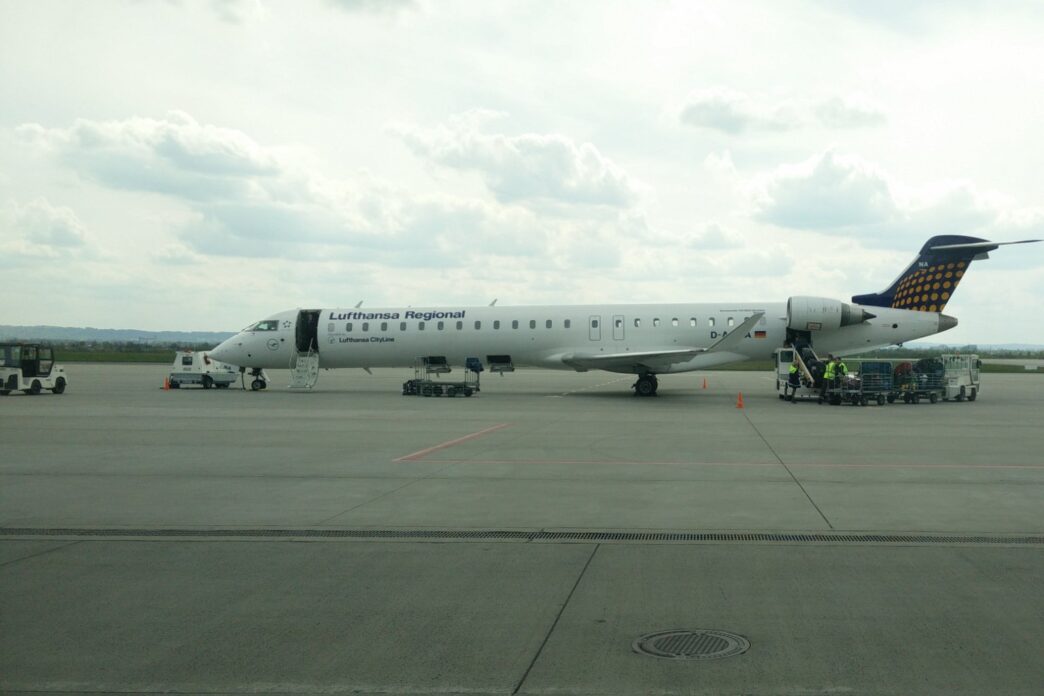Регіональний реактивний літак у ліврі Lufthansa Regional на пероні аеропорту Жешув-Ясьонка, поруч наземний персонал і обслуговуюча техніка