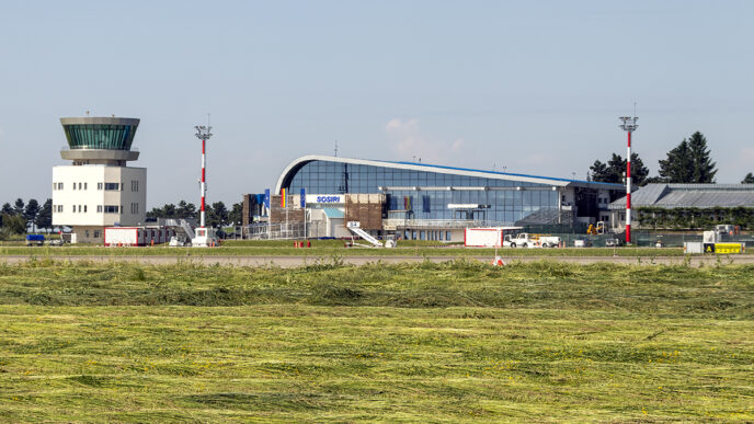 Скляний пасажирський термінал і диспетчерська вежа аеропорту Сучава, на передньому плані скошена трава льотного поля, ясний день