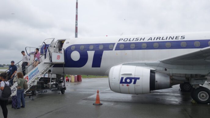 Пасажири спускаються трапом із реактивного літака у ліврі LOT на пероні аеропорту в похмуру погоду