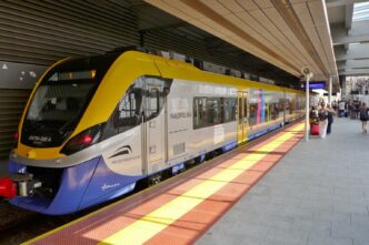 Приміський потяг Koleje Małopolskie стоїть біля платформи станції Kraków Lotnisko під навісом, на пероні праворуч пасажири