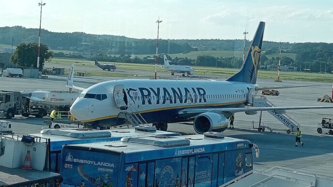Літак Boeing 737 у ліврі Ryanair біля телетрапа на пероні аеропорту Краків-Балиці, поруч перонний автобус і наземний персонал, денне світло