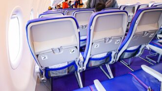 Ряди економ-крісел із фіолетовою оббивкою в салоні Airbus A321neo Wizz Air, вигляд ззаду на спинки сидінь, у проході пасажири під час посадки, денне світло