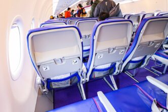 Ряди економ-крісел із фіолетовою оббивкою в салоні Airbus A321neo Wizz Air, вигляд ззаду на спинки сидінь, у проході пасажири під час посадки, денне світло